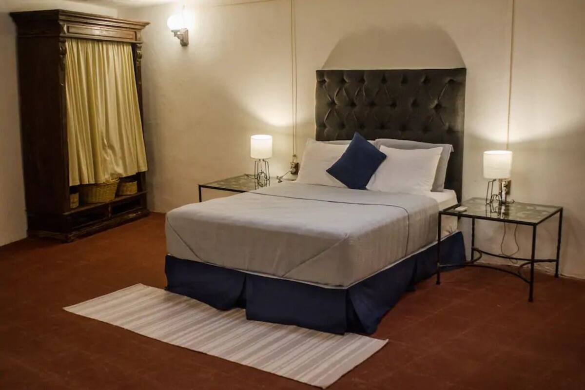 Una habitación de hotel con una cama grande, dos mesitas de noche con lámparas, un cabecero oscuro y un armario de madera.