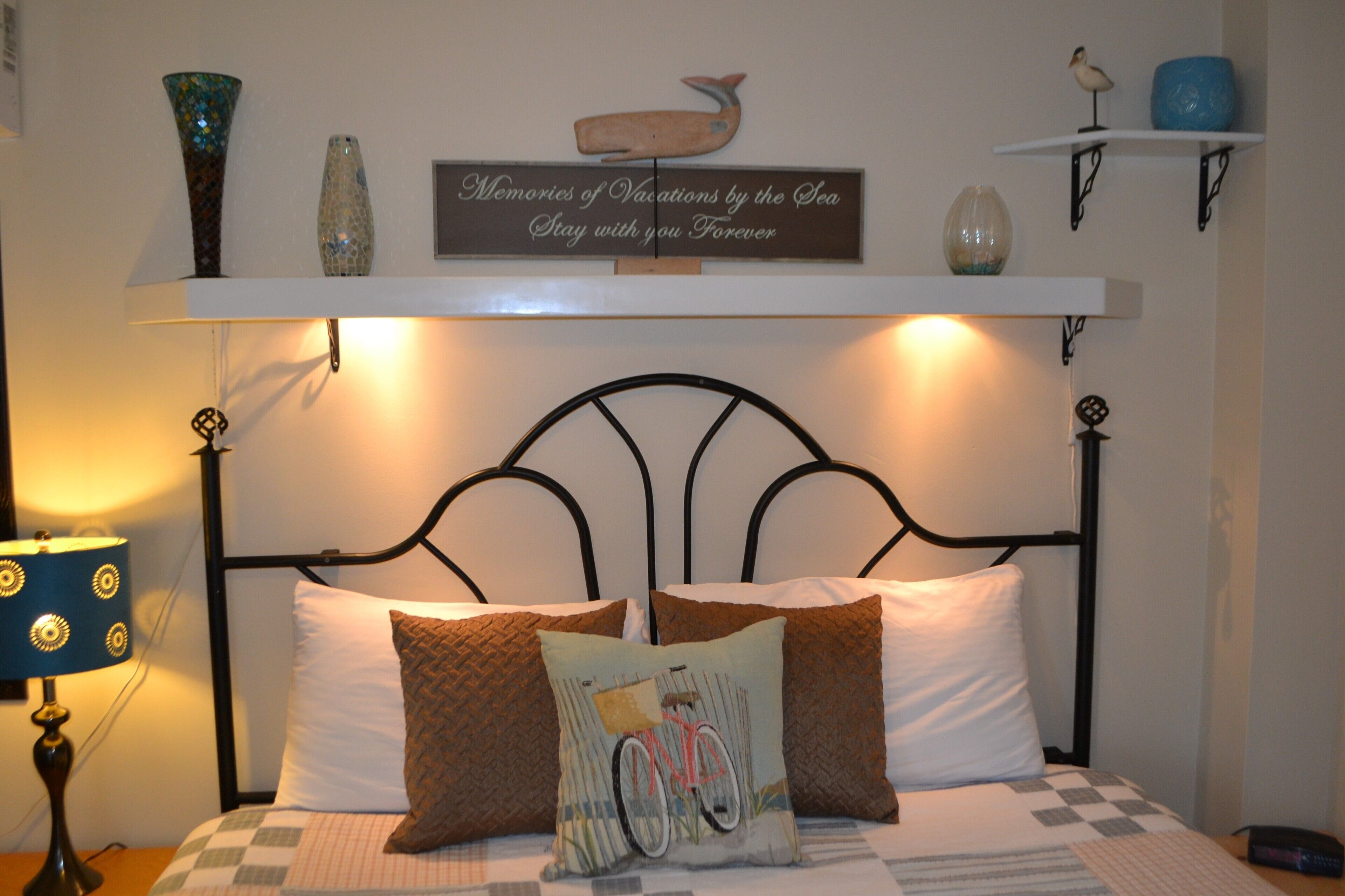 A neatly arranged bedroom with a bed, pillows, a lamp, and decorative items on shelves.