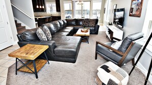 Ein modernes Wohnzimmer mit einem Ecksofa, einem Couchtisch und einem Fernseher. Eine Treppe führt zu einer oberen Ebene.