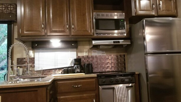 A kitchen with wooden cabinets, a stainless steel microwave, a refrigerator, a stove, and a coffee maker. - Family Time at Hills Hocking @ Pine Creek Villas: Creek Front (Rockbridge)