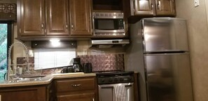 A kitchen with wooden cabinets, a stainless steel microwave, a refrigerator, a stove, and a coffee maker. - Family Time at Hills Hocking @ Pine Creek Villas: Creek Front (Rockbridge)