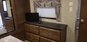 A compact RV interior with a kitchenette, a small TV on a dresser, and a window with curtains. - Family Time at Hills Hocking @ Pine Creek Villas: Creek Front (Rockbridge)