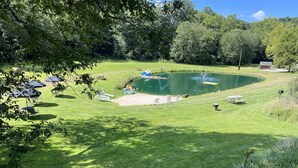 A grassy area with a pond, picnic tables, and umbrellas. - Family Time at Hills Hocking @ Pine Creek Villas: Creek Front (Rockbridge)