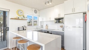 Eine moderne Küche mit einer großen Kochinsel, weißen Schränken, einer eingebauten Mikrowelle und einem Samsung-Kühlschrank.