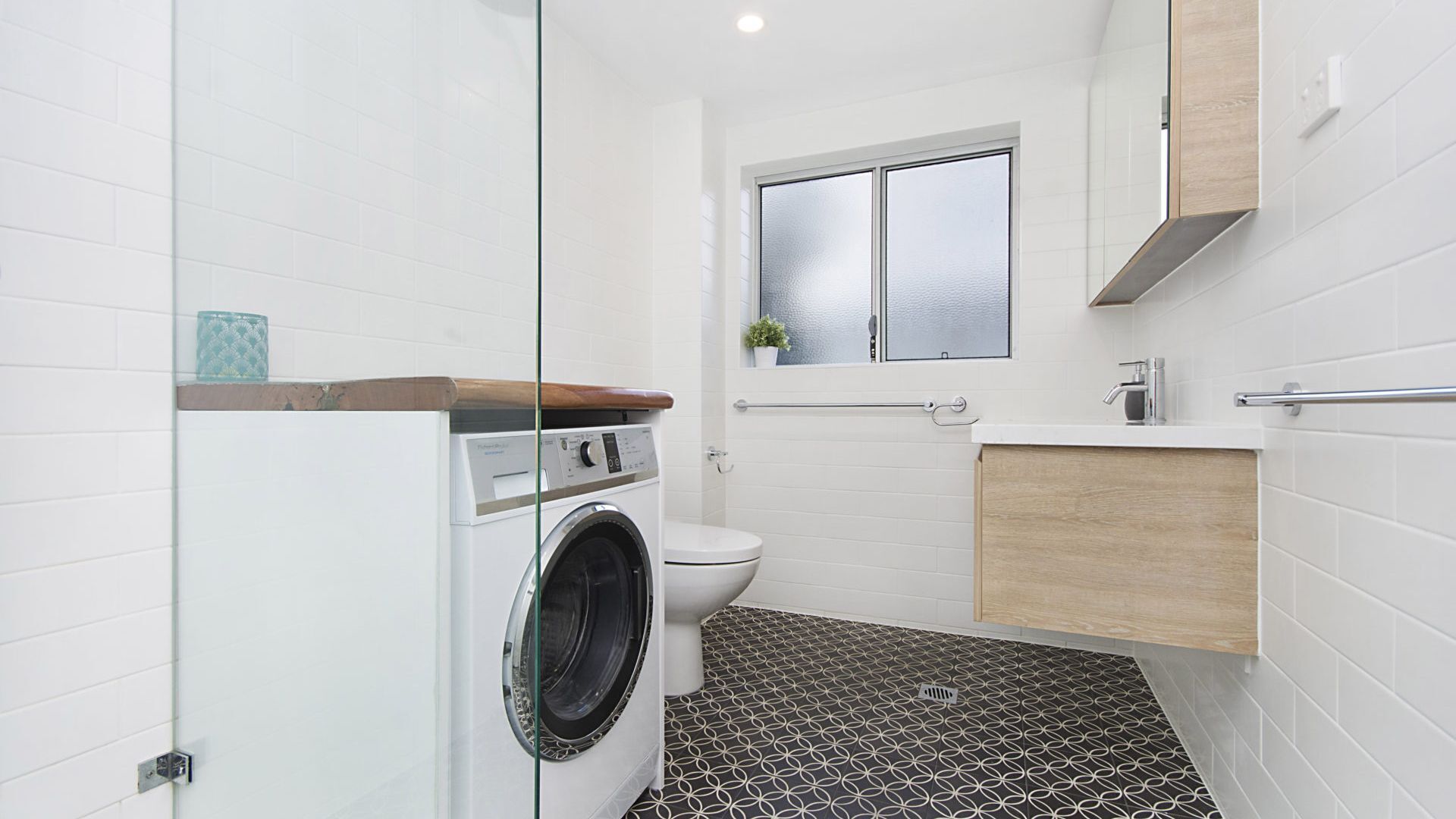A compact bathroom with a washing machine, toilet, and a small window.