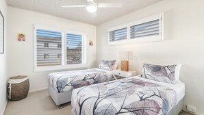Ein Schlafzimmer mit zwei Betten, einem Deckenventilator und großen Fenstern mit Jalousien.