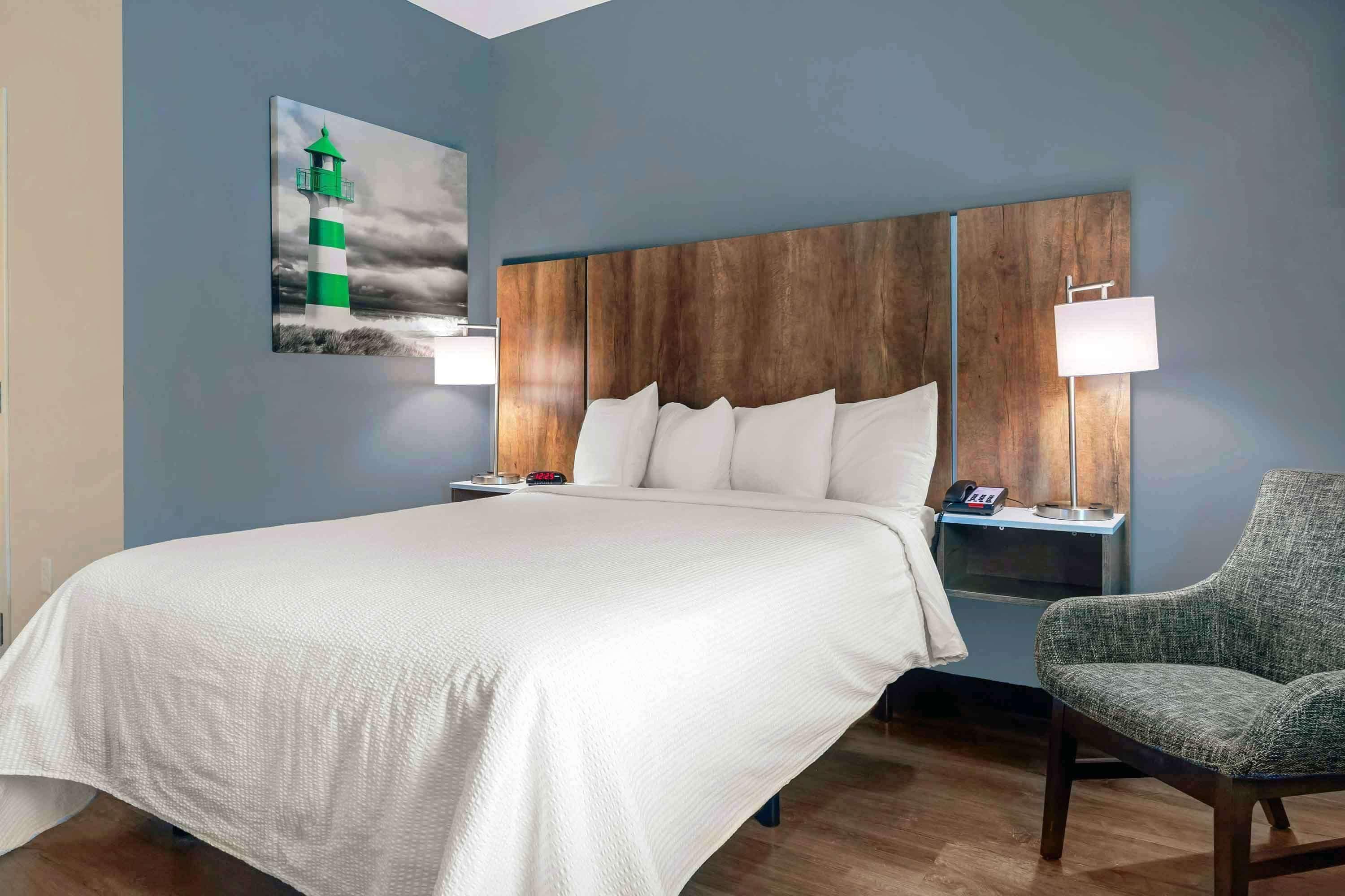Una cama bien hecha con sábanas blancas, un cabecero de madera y dos lámparas de noche.