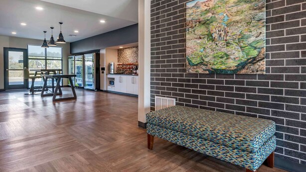 A spacious room with a wooden floor, a bench, a large abstract painting, and a kitchen area with a bar. - Extended Stay America Premier Suites Tampa Gibsonton Rivervi (Gibsonton)