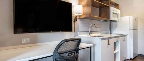 Una cocina compacta con televisor de pantalla plana, microondas, refrigerador y una silla.
