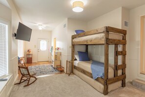 Een slaapkamer met een stapelbed, een televisie aan de muur, een schommelstoel en een klein bureau met stoel.