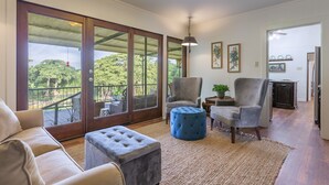 A spacious living area with a large sliding glass door leading to a balcony, a grey armchair, a blue ottoman, and a small table with a plant.