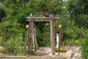 A rustic wooden archway with metal decorations and a pathway leading through a garden.