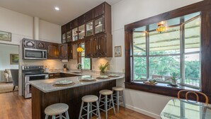 A kitchen with a central island, bar stools, a dining table, and a large window with a view.