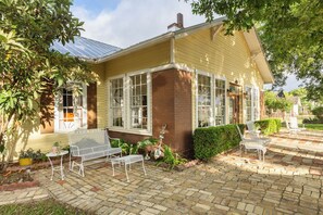 A yellow house with a brick foundation, large windows, and a covered patio area with outdoor furniture.