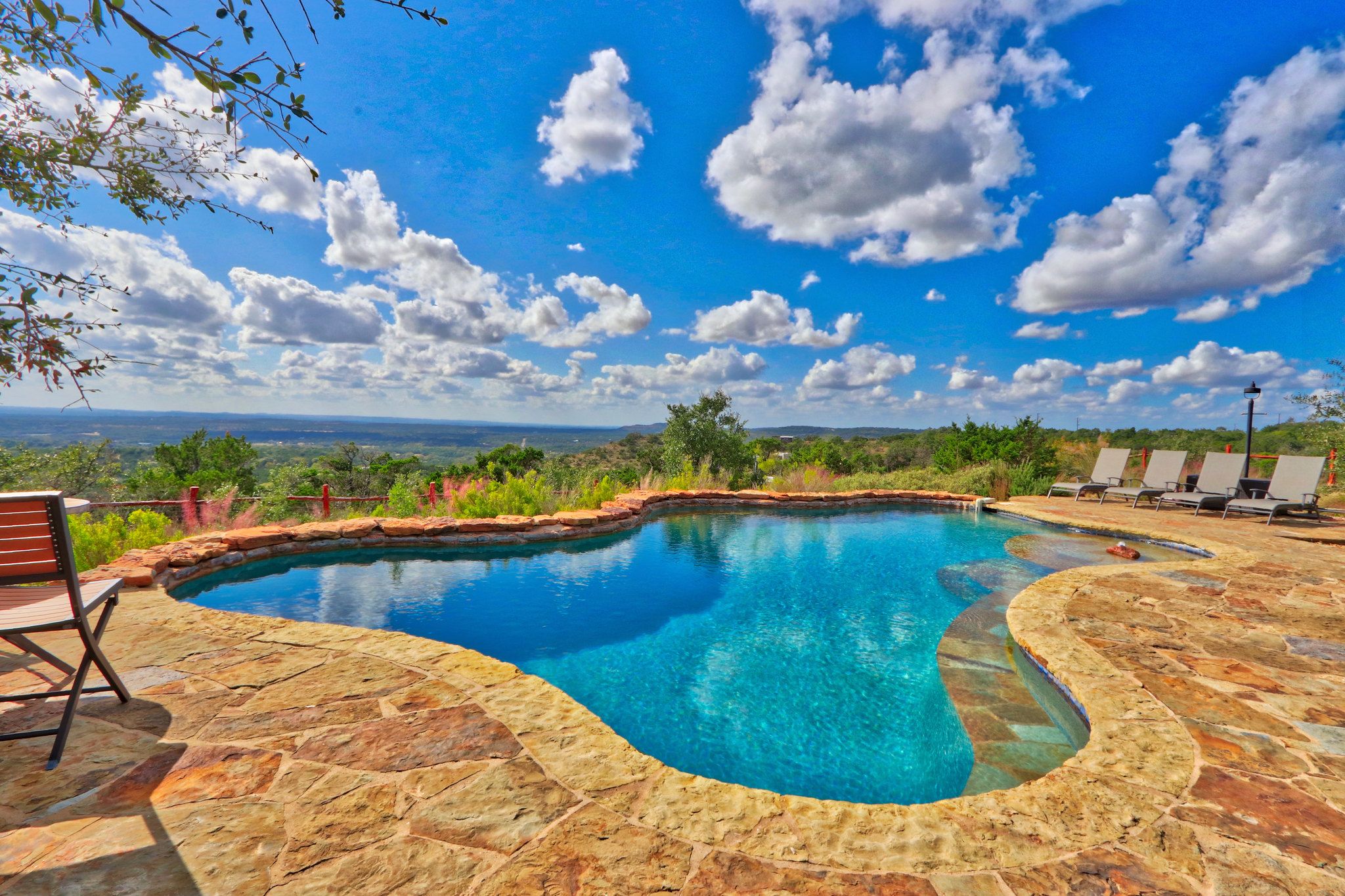 Una piscina con solárium de piedra, rodeada de sillones de descanso y vistas al paisaje.