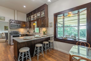 A kitchen with a central island, bar stools, a dining table, and a large window with a view.