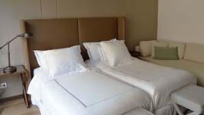 Un lit bien fait, avec du linge de lit blanc et des oreillers, une lampe de chevet et un coussin vert sur un canapé beige.