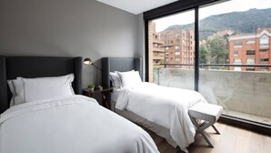 Une chambre d’hôtel moderne avec deux lits, une grande fenêtre et une vue sur les bâtiments et les collines.