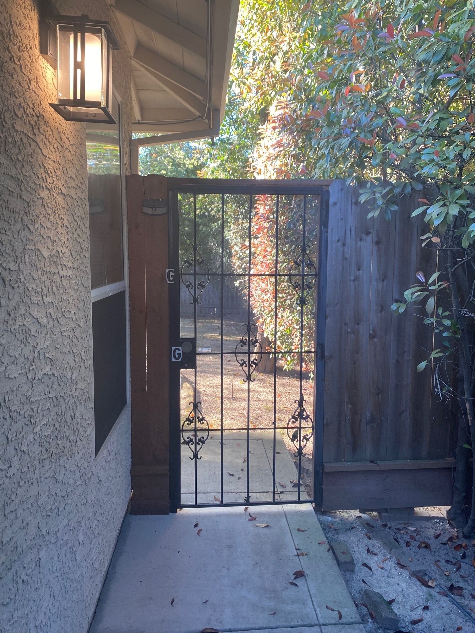 A gated entrance with a metal gate, a concrete pathway, and a wooden fence.