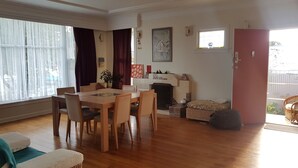 A spacious living room with a wooden dining table and chairs, a fireplace, and a large window with sheer curtains. - Character home, city close (Inner Kaiti)