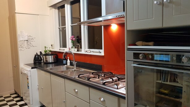 A kitchen with a gas stove, sink, and white cabinets. There is a window above the sink and a clock on the wall. - Character home, city close (Inner Kaiti)