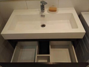A bathroom with a white sink, a soap dish, and a drawer.