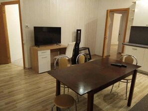 A compact living space with a wooden dining table, a TV, a small kitchenette, and a desk with a chair.
