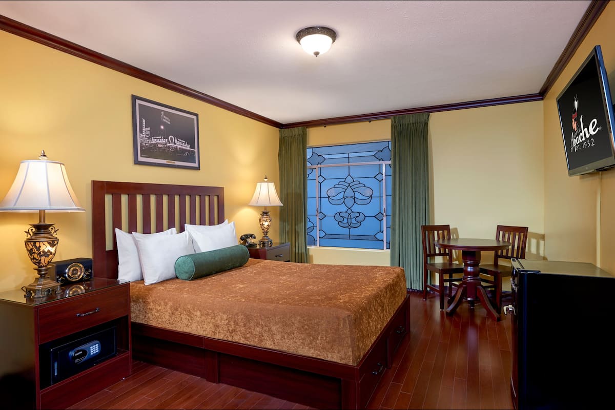 A hotel room with a bed, bedside lamps, a desk with a chair, a TV, and a window with curtains.