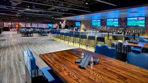 Een moderne bar met verschillende zithoeken, een houten bar en meerdere schermen die iets tonen.