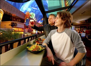 A restaurant with a view of a neon-lit building and a large screen displaying an image of a person. - Hotel Apache (Las Vegas)