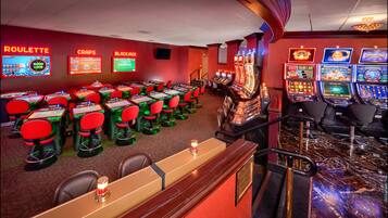 A casino floor with multiple gaming tables and slot machines, including roulette, craps, and blackjack.