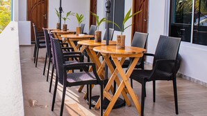 Un espace extérieur aménagé avec des tables rondes en bois et des chaises en osier noir, le tout à l’ombre de grands parasols.