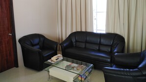 Un salon avec une table basse en verre, deux fauteuils en cuir noir et un canapé beige.