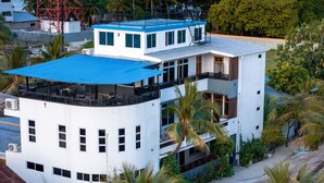 Un hôtel à plusieurs étages, doté de balcons, d’un toit bleu et entouré de palmiers.