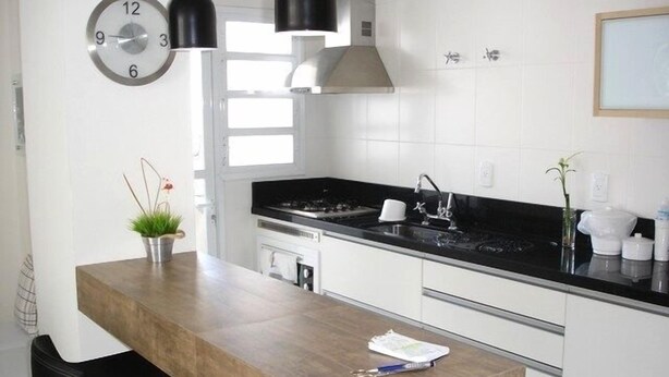 Una cocina moderna con encimera de madera, lámparas colgantes negras, un lavamanos de acero inoxidable y armarios blancos.
