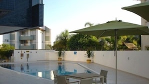 Piscina exterior con mesa y sillas, rodeada por un muro blanco y follaje.