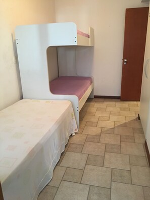 Une petite pièce avec un lit superposé et un lit simple. Il y a une porte sur le côté droit.