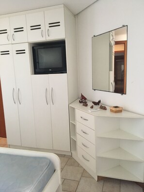 A bedroom with a bed, a white wardrobe with multiple compartments, a television, a mirror, and a small table with decorative items.