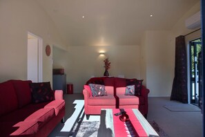 A living room with two red sofas, a coffee table, and a wall-mounted clock. - Okareka Escape - Lake Views & Lakeside Walk (Rotorua)