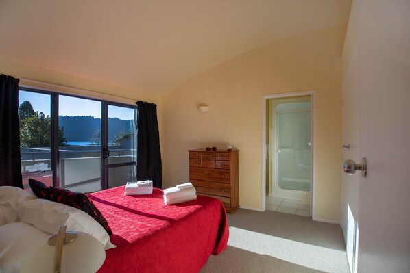 A bedroom with a bed, a dresser, a door, and a view of the outdoors.