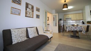 A living room with a sofa, a dining table with chairs, a kitchen area, and a hallway. - Avilés-Salinas V. U.T. 612-AS (salinas/castrillon)
