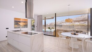 Una cucina moderna con piano di lavoro in marmo, cappa aspirante in acciaio inossidabile e un'ampia finestra con vista su piscina e montagne.
