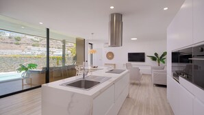 Cucina moderna con isola centrale ampia, elettrodomestici in acciaio inox e vista su piscina e colline.