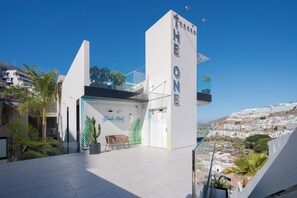 A modern building with a prominent 'THE ONE' sign, a glass balcony, and a view of a coastal cityscape.