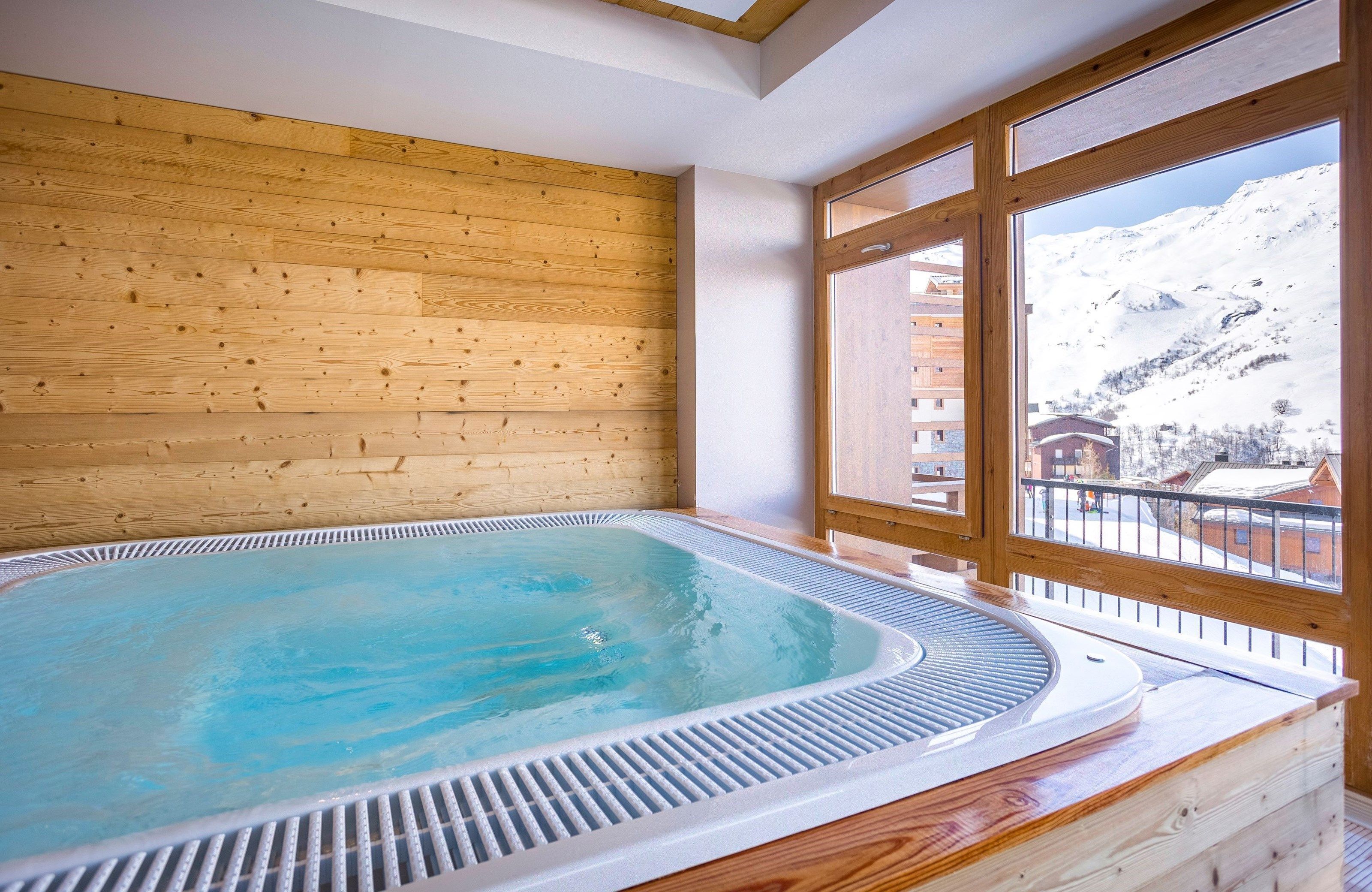 Une pièce aux murs lambrés, dotée d’un jacuzzi et d’une grande fenêtre donnant sur une montagne enneigée.