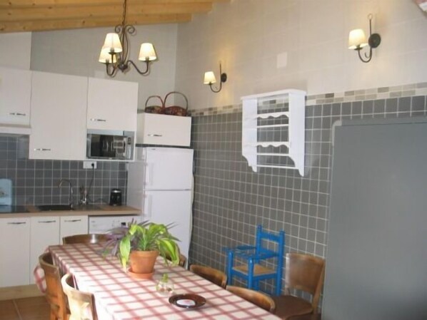 A kitchen with white cabinets, a microwave, a refrigerator, and a tiled backsplash. There is a dining table with chairs and a potted plant.