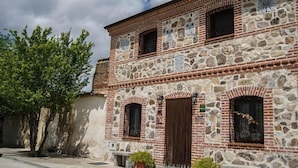 Un bâtiment en pierre doté de fenêtres en arc de cercle et d’une porte en bois, entouré d’arbres.