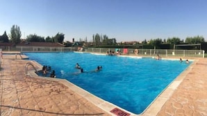 Une piscine à l’eau d’un bleu cristallin, entourée d’une terrasse en pierre et d’une clôture en métal.