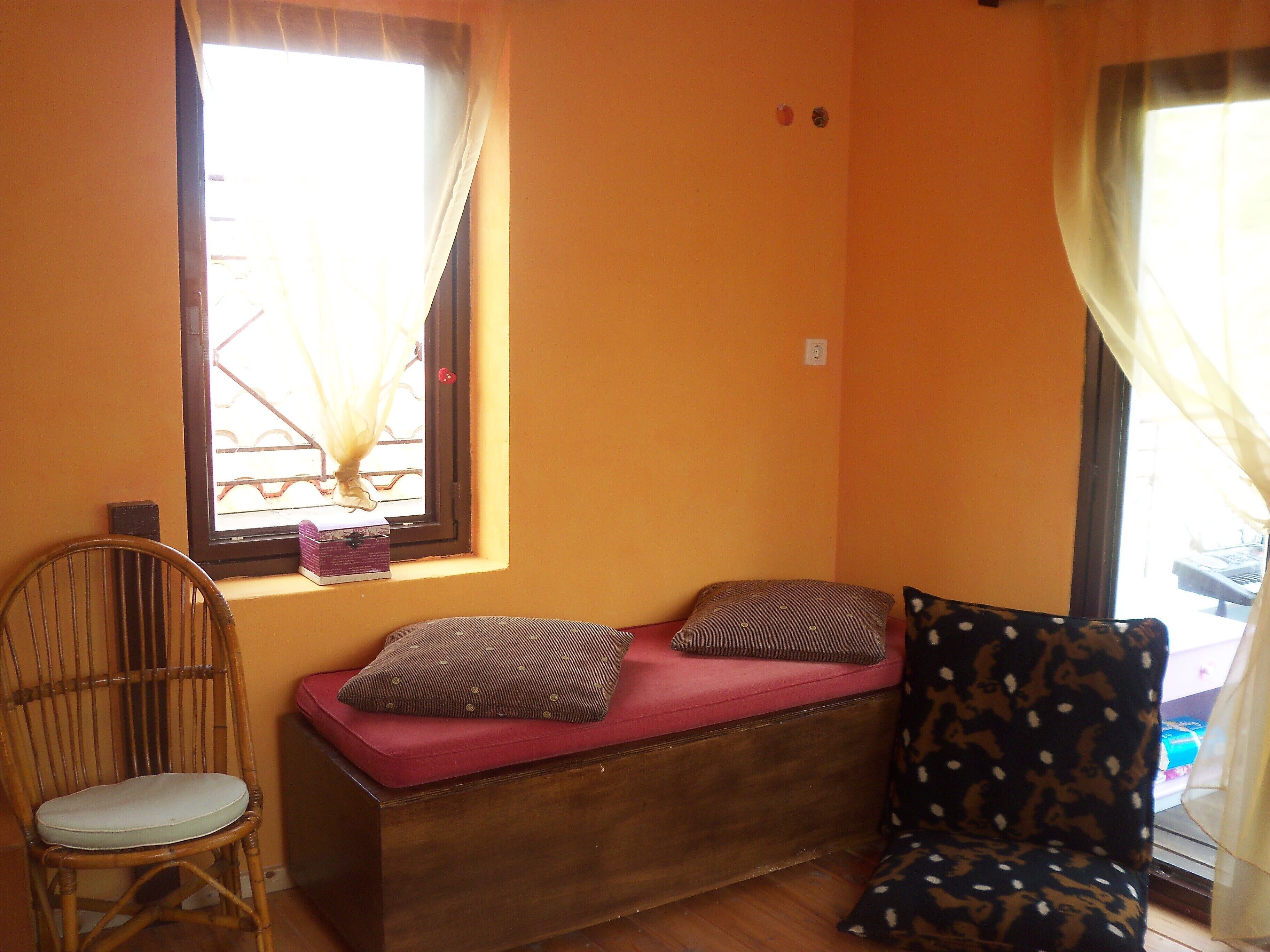 A room with a wooden bench, a wicker chair, and a window with curtains.