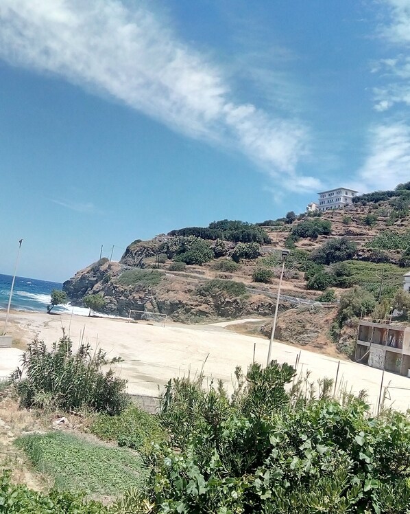 Un paisaje costero con playa, terreno rocoso y un edificio en una colina.
